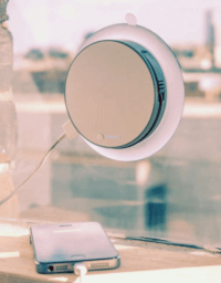A picture of a white cicular plastic charger stuck to a window with a large suction cup, connected to a mobile phone via a cable
